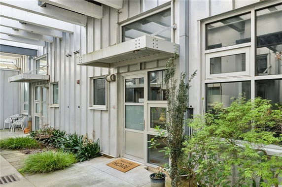Front view of a modern industrial-style building with large windows and plants at the entrance.