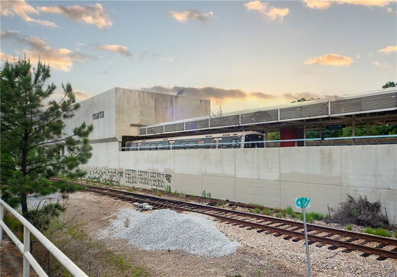 Front view of a transit station with a train and graffitied walls.
