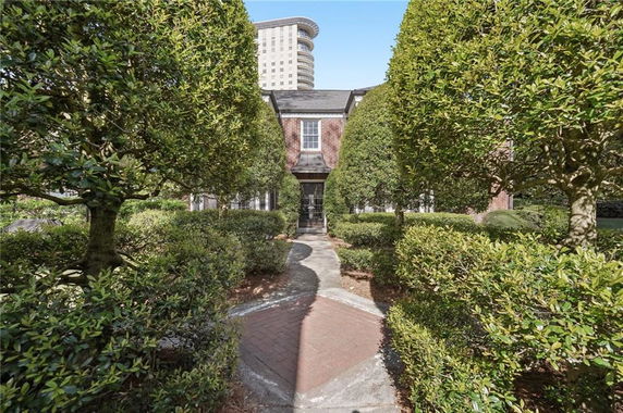 Front view of a brick house with a walkway lined by neatly trimmed bushes and trees.