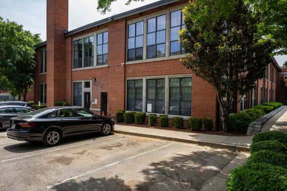 Front view of a two-story brick building with large windows and a parking area in front.