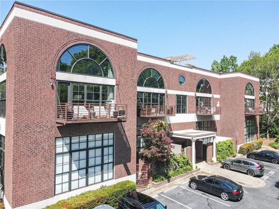 Front view of a three-story brick building with large arched windows and a parking area in front.