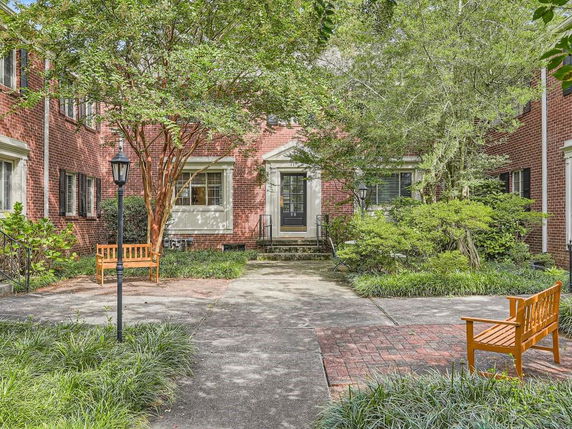 Front view of a red brick building with a central entrance, surrounded by trees and benches.
