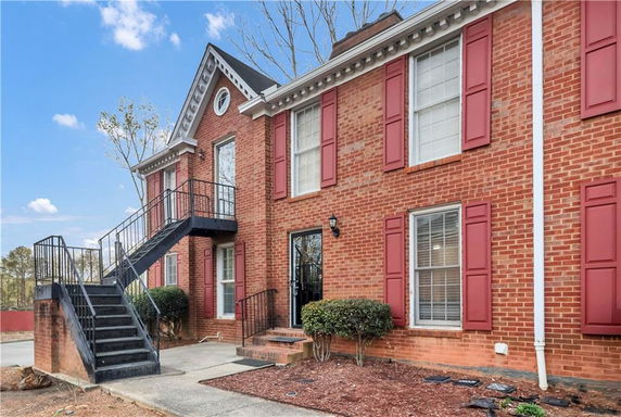 Front view of a red-brick building with red shutters and an external staircase.