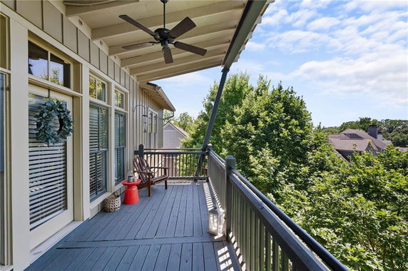 View from a balcony with seating and ceiling fan, overlooking trees and neighboring houses.