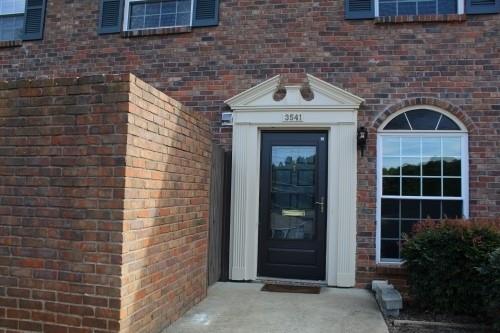 Front view of a brick house entrance with a decorative door frame and adjacent windows.