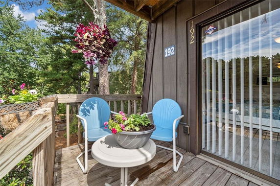 Outdoor deck area with two blue chairs, a small table with a plant, and a view of trees.