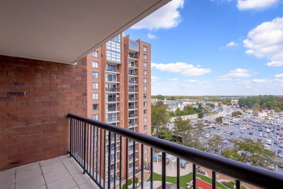 View from a balcony overlooking a multi-story building and a parking area in the distance.