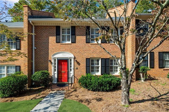 Front view of a two-story brick house with a red door and black shutters.