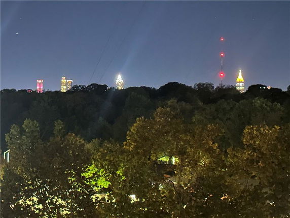Nighttime panoramic view of a city skyline with illuminated buildings and a red-lit antenna.