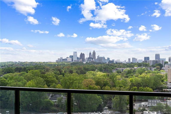 Panoramic view of a city skyline from a balcony, overlooking a forested area.