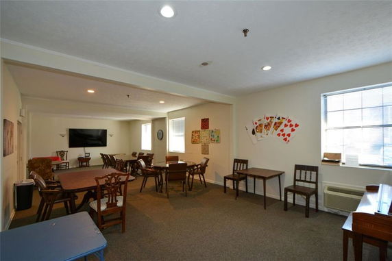 Room with tables and chairs for recreational activities, wall decorations and a television.