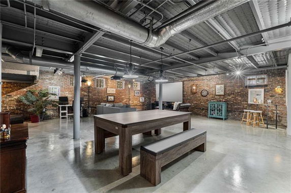 Interior view of a basement clubhouse with brick walls, featuring a table, benches, and various recreational areas.
