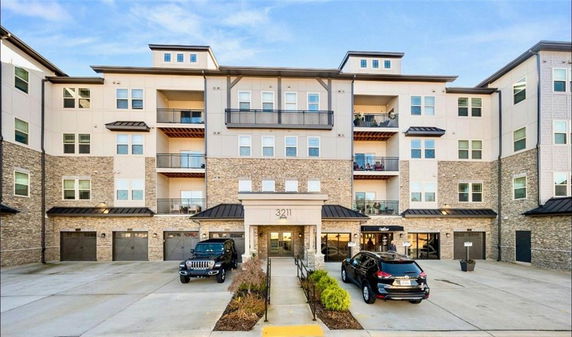 Front view of a multi-story apartment building with a central entrance and parking in front.