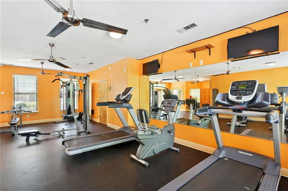 Indoor gym area with exercise equipment, mirrors, and ceiling fans.