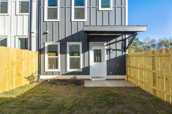Rear view of a modern two-story townhouse with a fenced yard.