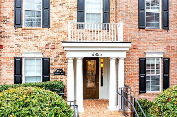Front view of a brick house with black shutters and a columned entrance.