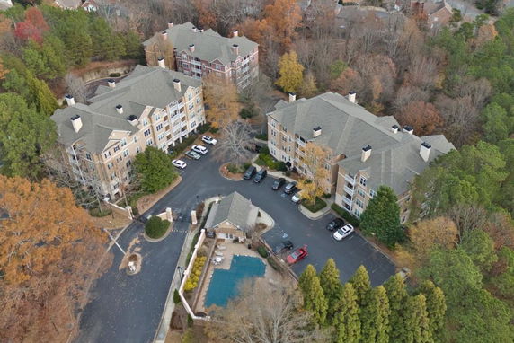 Aerial view of multiple residential buildings surrounded by trees and a parking area.