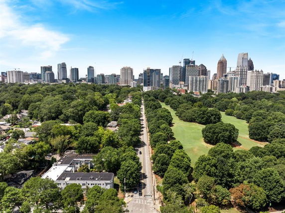 Panoramic view of a city skyline with a park and tree-lined road in the foreground.