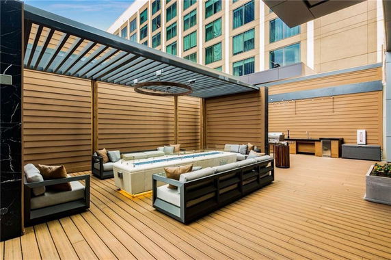 Outdoor seating area with sofas under a pergola, featuring a barbecue grill and dining space.