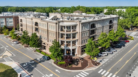 Front view of a multi-story building with balconies and ground floor entrances on a street corner.