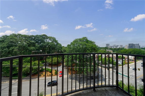 A view from a balcony overlooking a tree-lined road and distant buildings.