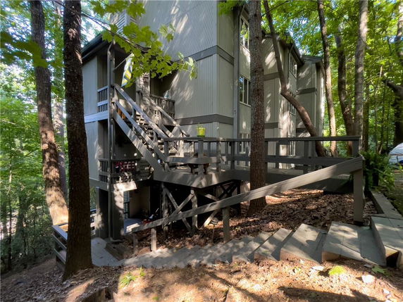 Front view of a multi-story house with stairs and wooden railings surrounded by trees.