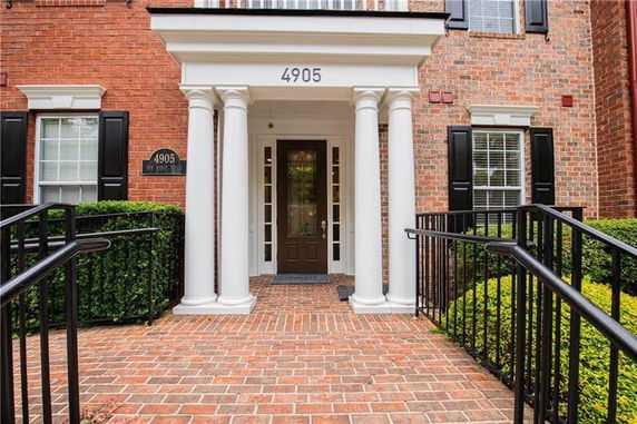 Front view of a brick building entrance with white columns and black shutters.