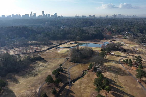 Wide angle aerial view of a landscape with a golf course and a distant city skyline.