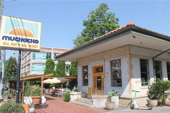 Front view of a single-story building with a sign reading 'Muchacho' and outdoor seating area.