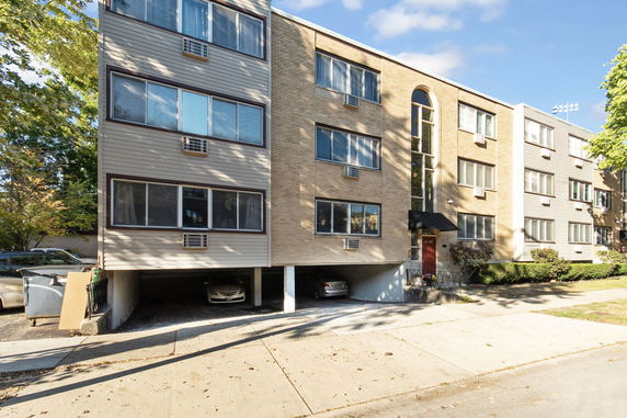 Front view of a multi-story apartment building with garages below and large windows.