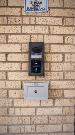 Front view of a building with a security panel and mailbox on a brick wall.