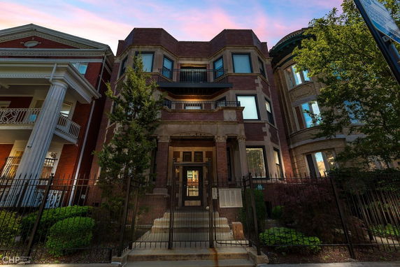 Front view of a multi-story brick building with a balcony and decorative columns.