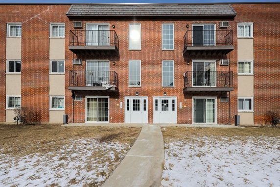 Front view of a three-story brick apartment building with balconies and white doors.