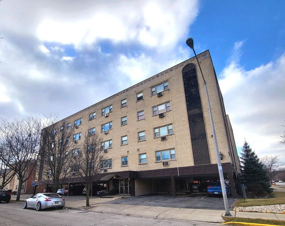 Front view of a multi-story brick building with parking spaces at the ground level.