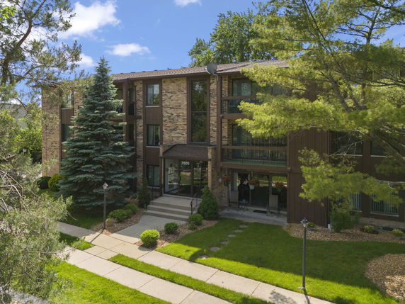 Front view of a multi-story brick building with large windows and a landscaped entrance.