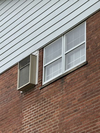 Close-up view of a building's exterior with brick and siding walls and a window air conditioning unit.