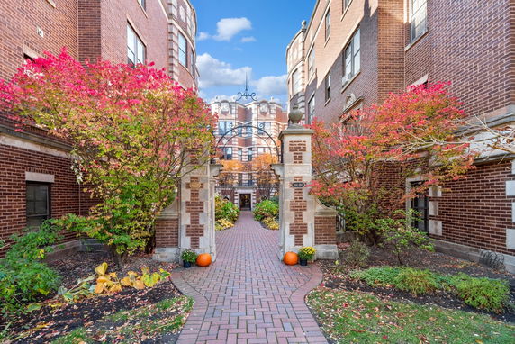Front view of a brick building with a decorative archway and autumn-colored foliage.