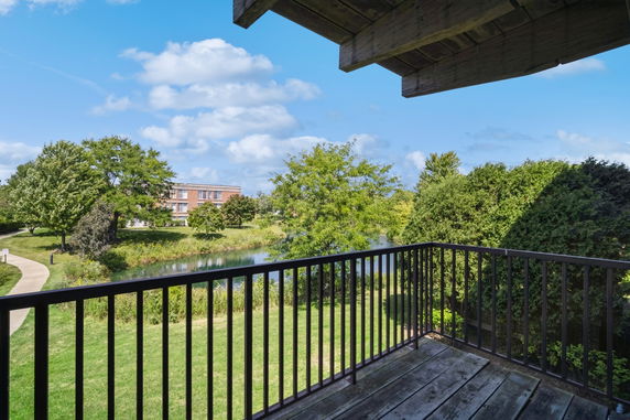 View from a balcony overlooking a grassy area with trees and a building in the distance.