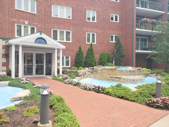 Front view of a multi-story brick building with an entrance featuring columns and a decorative water feature.