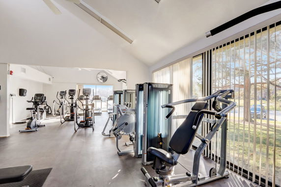 Indoor fitness area with various exercise machines and large windows.