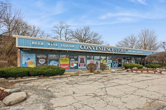 Front view of a convenience store with large signage and multiple advertisements on the windows.