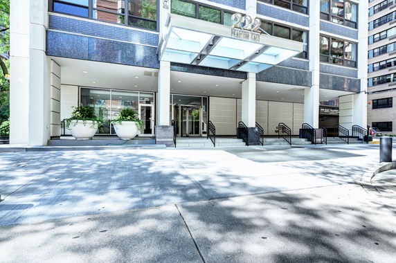 Front view of a modern multistory building entrance with large planters and a covered entryway.