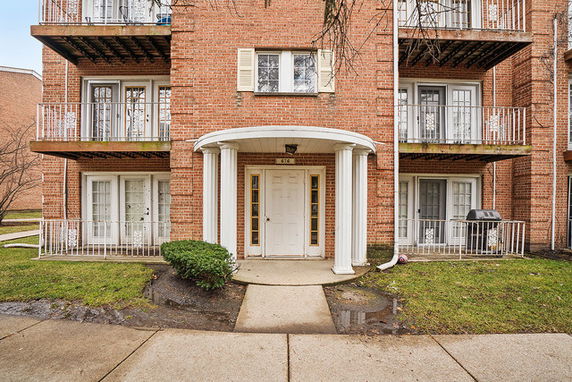 Front view of a brick apartment building with balconies and a central entrance with columns.