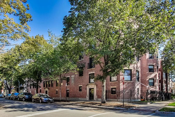 Front view of a multi-story brick building with multiple windows and trees surrounding it.