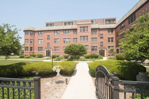 Front view of a multi-story brick apartment building with landscaped entrance.