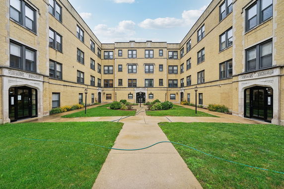 Front view of a multi-story brick apartment building with a courtyard.