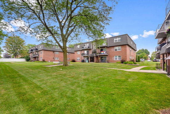 Front view of apartment buildings with multiple balconies and a large tree in the courtyard.