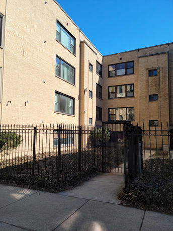Front view of a multi-story brick building with a black metal fence.
