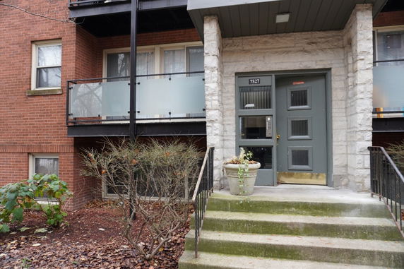 Front view of a multi-story brick building with a glass balcony and entry door.