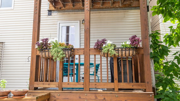 Front view of a wooden porch with decorative plants and a glass door.